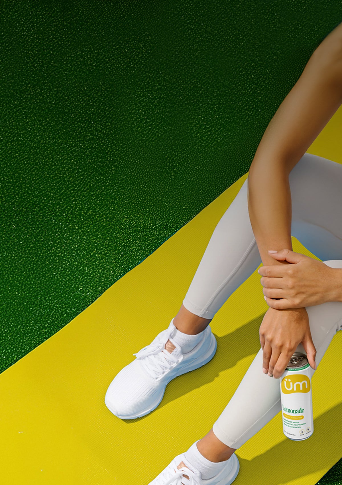 Woman sitting on a yellow yoga mat with Lemonade üm in her hand.